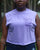 Person wearing a light purple sleeveless shirt with text, standing outdoors.